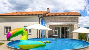 Ein Schwimmbecken mit Schwimmgelegenheiten, Sonnenschirmen und einem Haus mit Ziegeldach und Steinverkleidung.