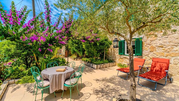 A patio with a round table and chairs, a stone wall, and flowering plants.