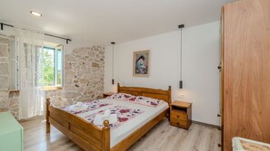 A bedroom with a wooden bed, a nightstand, a stone wall, a painting, and a window with curtains.