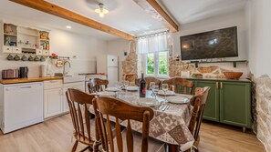 A dining area with a table set for four, a kitchen with white appliances, a stone wall, and a flat-screen TV mounted above a green cabinet.