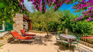 A patio with a table and chairs, a stone wall, and a view of a garden with trees and flowers. - Guest House Sunset Kalla by Villas Guide (Rab)