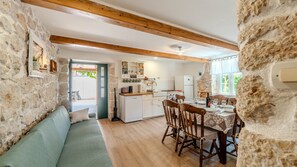 A cozy room with a wooden ceiling, stone walls, a dining table with chairs, a kitchen area, and a sofa.
