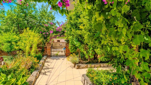 A garden pathway leading to a brick gate, surrounded by lush greenery and flowering plants. - Guest House Sunset Kalla by Villas Guide (Rab)