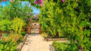 A garden pathway leading to a brick gate, surrounded by lush greenery and flowering plants.