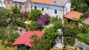 A stone building with a red roof, surrounded by lush greenery and purple flowers. - Guest House Sunset Kalla by Villas Guide (Rab)