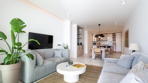 Ein modernes Wohnzimmer mit einem grauen Sofa, einem weißen Couchtisch und einer großen Pflanze in einem Topf.