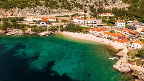 Luftaufnahme einer Küstenstadt mit Gebäuden, einem Strand und klarem türkisfarbenem Wasser.