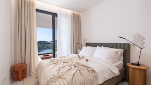 Ein Schlafzimmer mit Bett, Nachttisch, Lampe und Blick auf ein Gewässer.