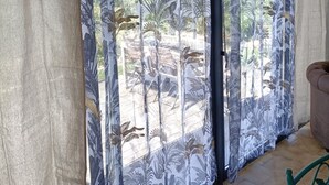 Een kamer met een groot raam voorzien van patroon gordijnen, een betegelde vloer en een groene stoel.