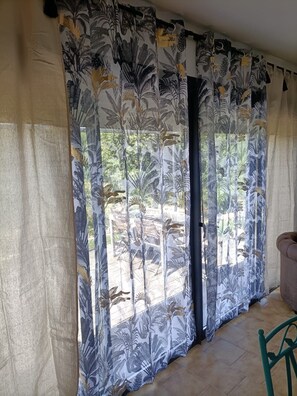 Ein Zimmer mit einem großen Fenster, das mit gemusterten Vorhängen verziert ist, einem gefliesten Boden und einem grünen Sessel.