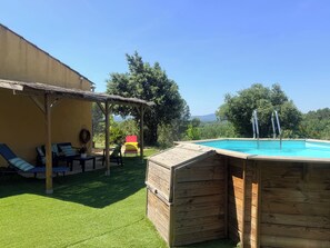 Eine Holzterrasse mit Pool, einer überdachten Sitzgruppe und Blick auf Bäume und Hügel.