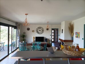 Ein modernes Wohnzimmer mit einem Glastisch, smaragdgrünen Sesseln, einer großen Wanduhr und einem Fernseher.