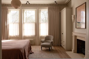 A bedroom with a bed, a chair, a fireplace, and large windows with curtains. - Period Townhouse - Garden Gym Playroom (London)