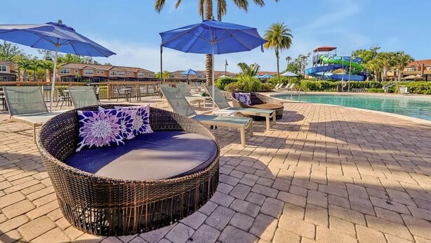 Un área junto a la piscina con sillones de mimbre, sombrillas y un tobogán acuático al fondo.