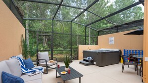 Un patio techado con sofá, sillones, una mesa, un jacuzzi y vistas del bosque circundante.