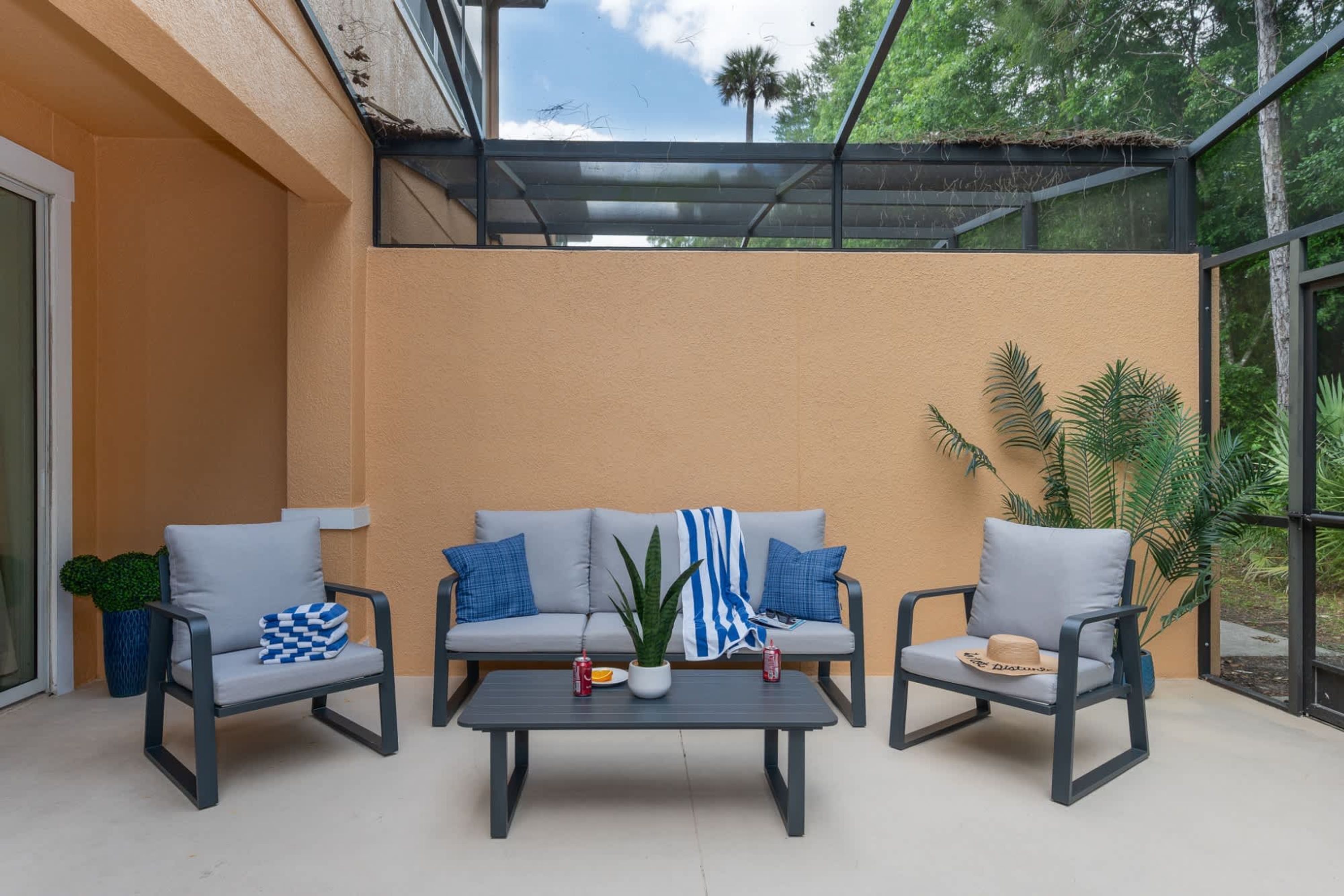 A covered patio with a sofa, two chairs, a table, and potted plants.