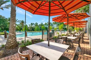 An outdoor patio area with tables and chairs, a pool, and palm trees. - 20 Mins to Disney Arcade Battles Mini Golf (Davenport)
