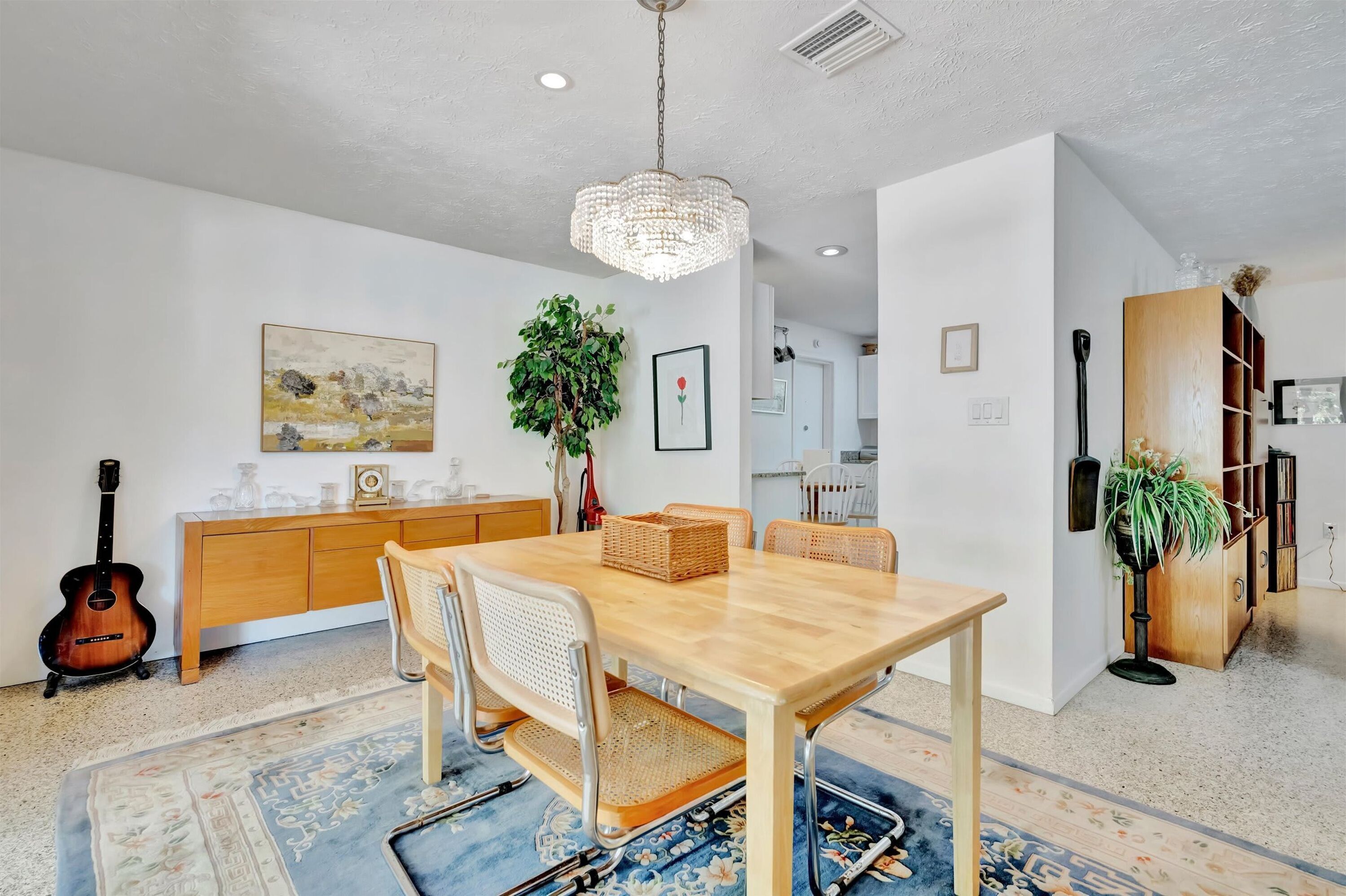 Un comedor con mesa de madera, sillas, candelabro, guitarra, aparador y planta.
