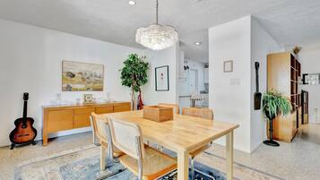 Un comedor con mesa de madera, sillas, candelabro, guitarra, aparador y planta.
