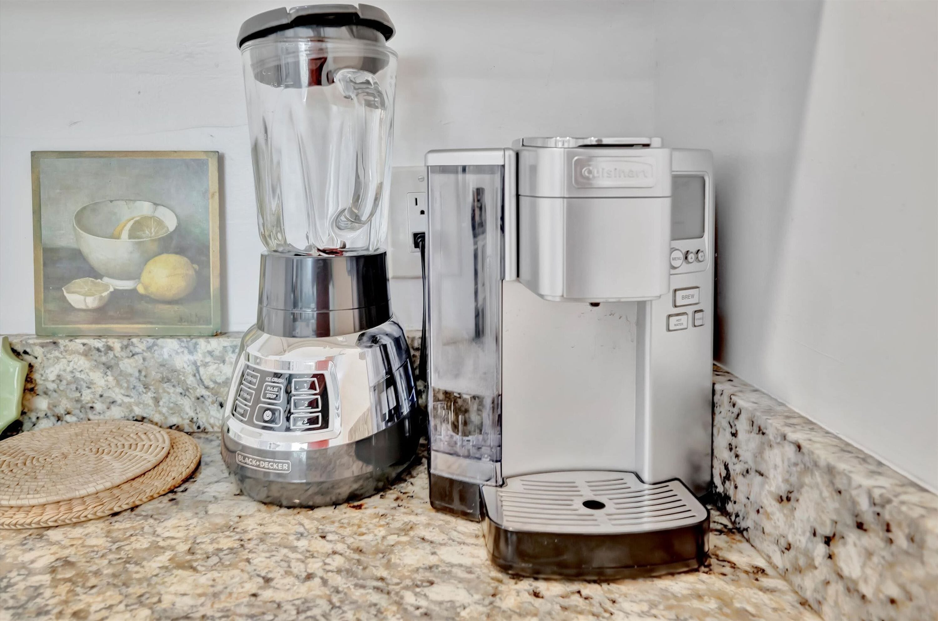 A kitchen with a blender, a coffee maker, and a framed picture of lemons.