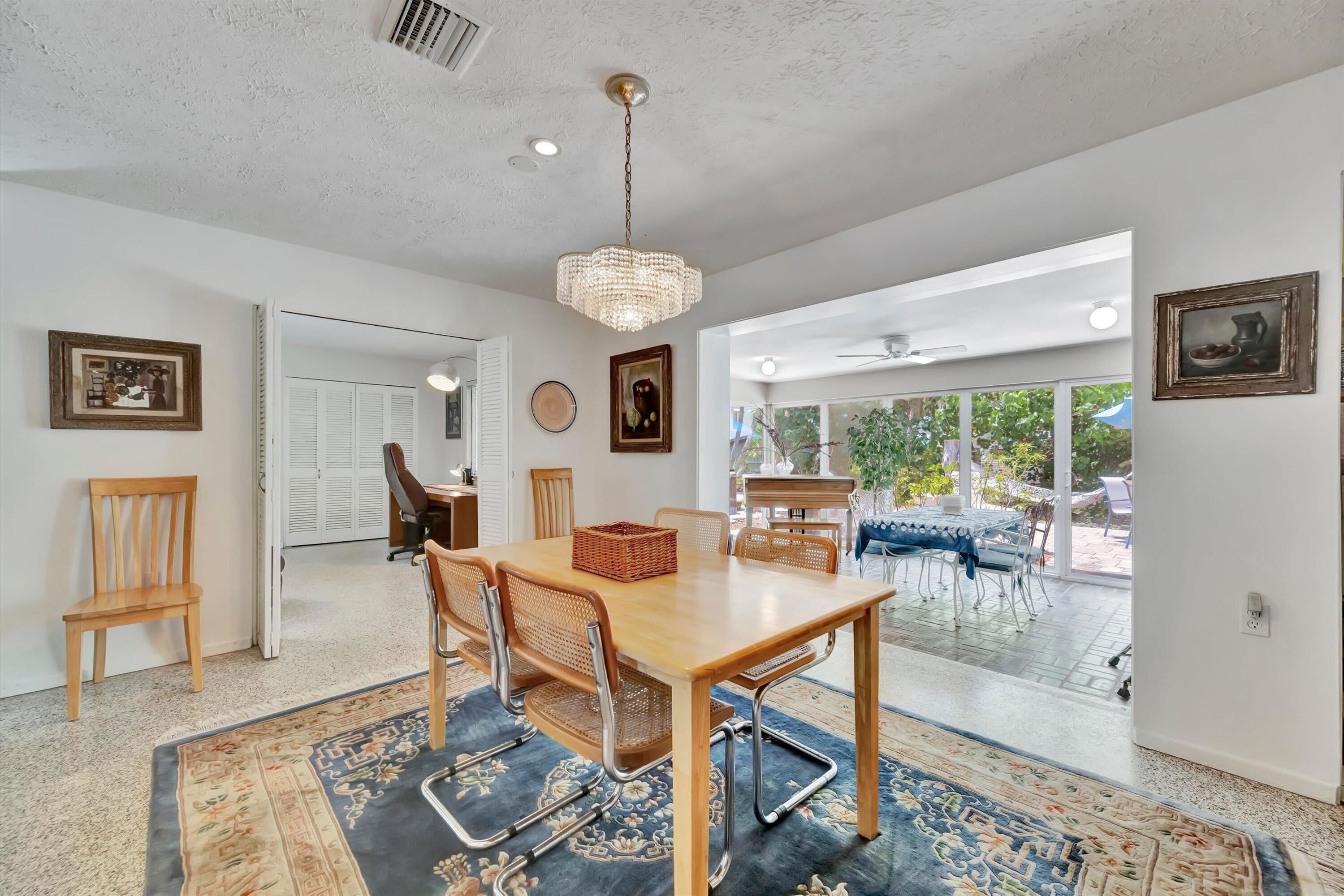 A dining area with a wooden table, chairs, a chandelier, and a view to the outside.