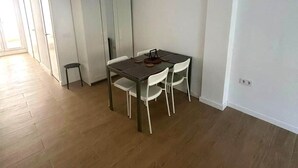 Ett rymligt rum med trägolv, ett matbord med stolar, en garderob och en liten pall.