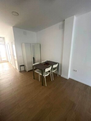 Een ruime kamer met houten vloer, een eettafel met stoelen, een kledingkast en een klein krukje.