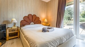 Hotellihuone, jossa on suuri sänky, puinen pääty, kaksi yöpöytävalaisinta, pieni puinen yöpöytä ja näkymä ulos.