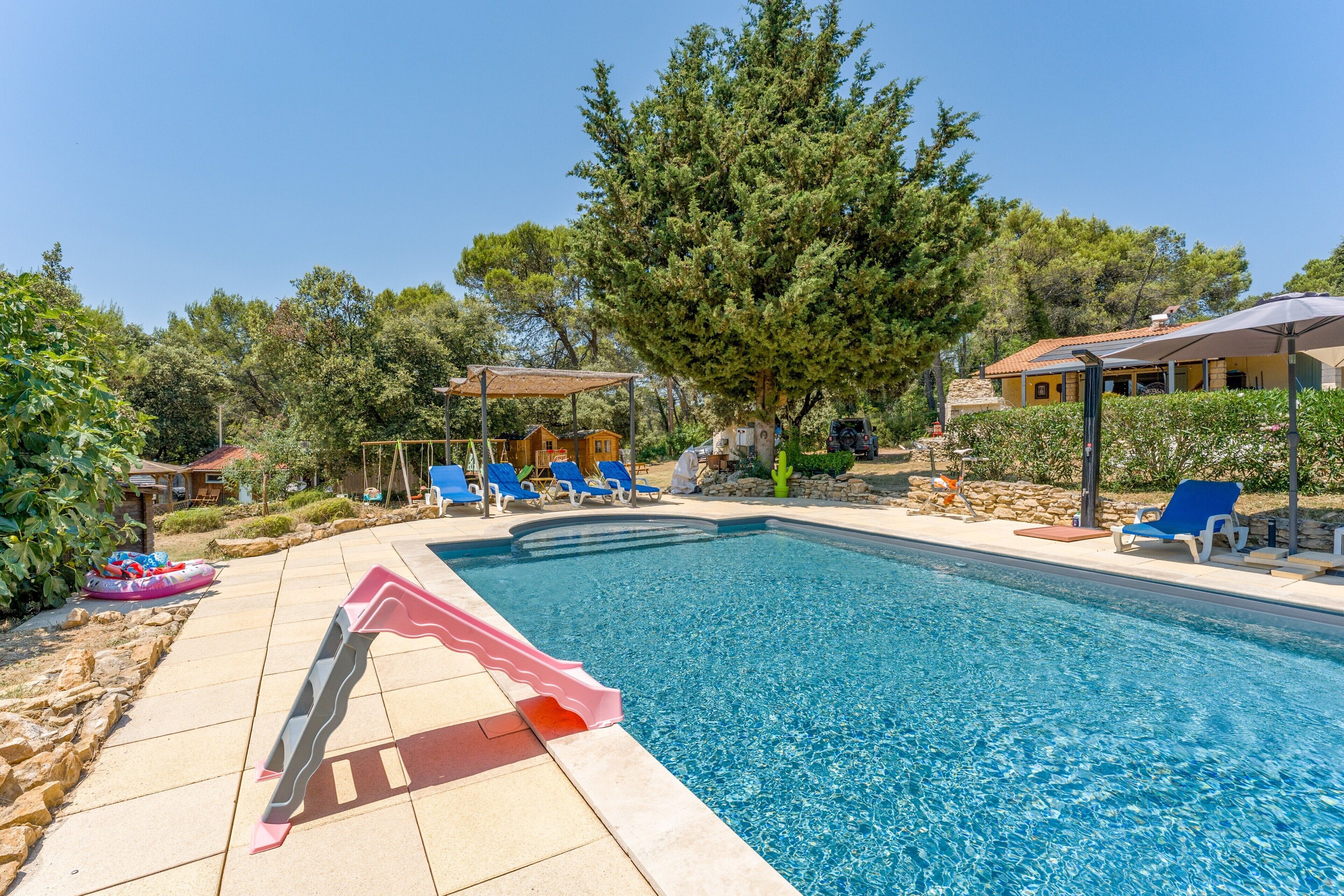 Una piscina con tobogán, sillas de descanso y una zona techada.