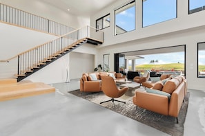Ein geräumiger Wohnbereich mit moderner Treppe, Ledersofas und großen Fenstern mit Blick ins Freie.