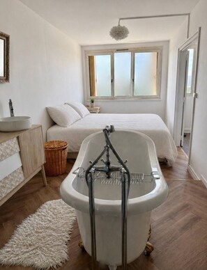 Ein modernes Schlafzimmer mit einer Badewanne, einem Bett, einem Fenster und einem kleinen Nachttisch.