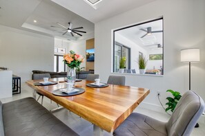 Ein moderner Essbereich mit Holztisch, grau gepolsterten Stühlen, einer Vase mit Blumen und einem großen Fenster mit Aussicht.
