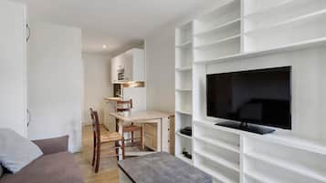 Un salon moderne avec un téléviseur à écran plat fixé sur une étagère blanche, une table à manger en bois avec des chaises et un canapé gris.