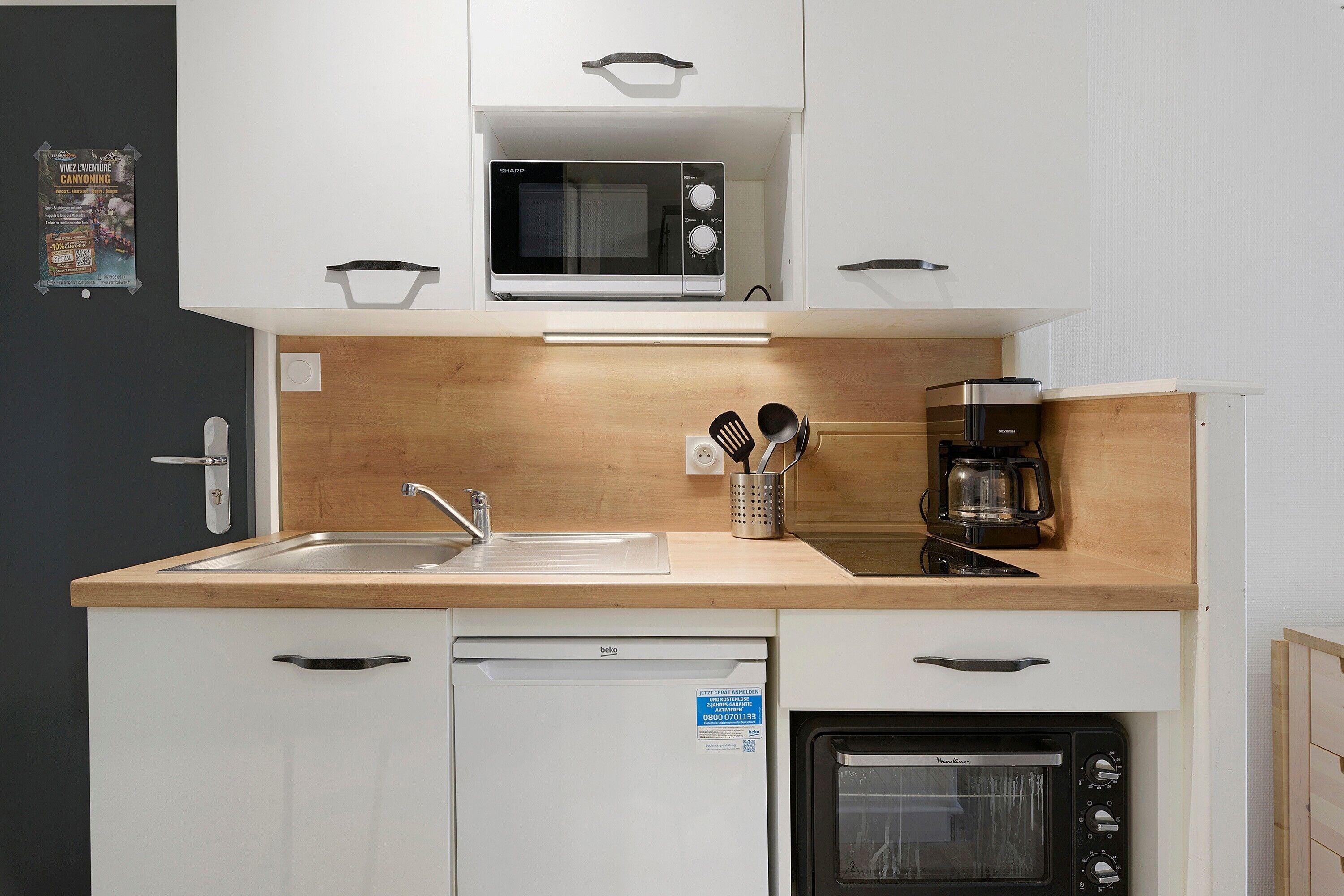 A compact kitchen with a microwave, coffee maker, and built-in oven.