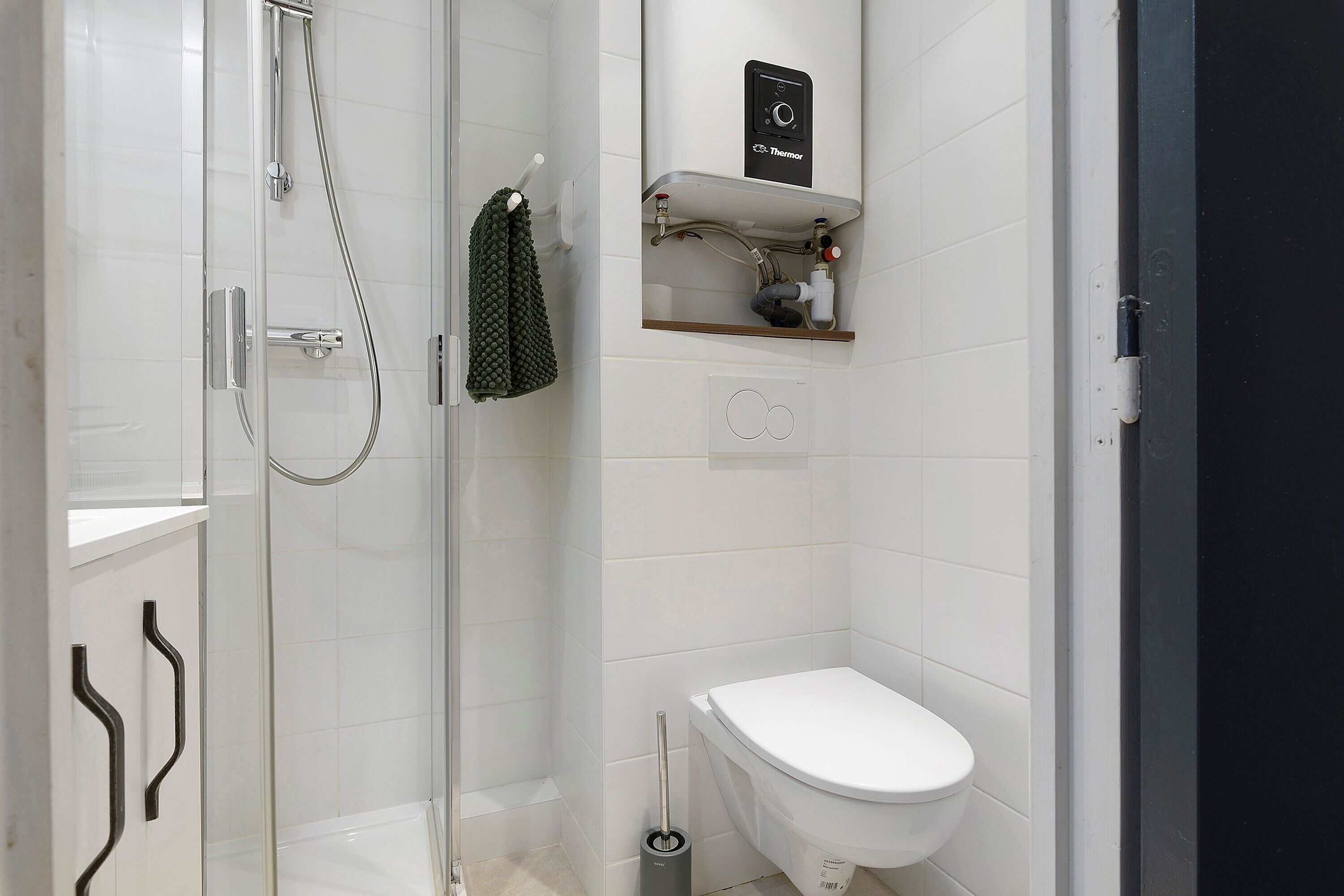 Une salle de bain moderne avec une douche à parois de verre, des toilettes blanches et une étagère contenant des articles de toilette.