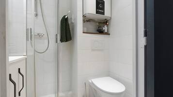 Une salle de bain moderne avec une douche à parois de verre, des toilettes blanches et une étagère contenant des articles de toilette.