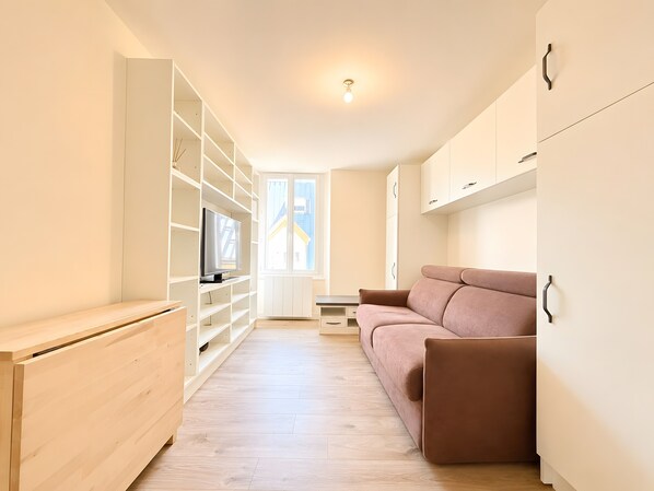 Eine moderne Wohnung mit Holzboden, einem braunen Sofa, weißen Einbauschränken und einem Fenster.