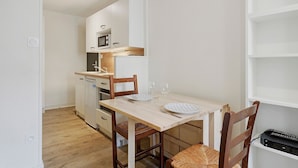 Cocina compacta con microondas, horno y un refrigerador pequeño. Hay una mesa de comedor con sillas y platos para dos.