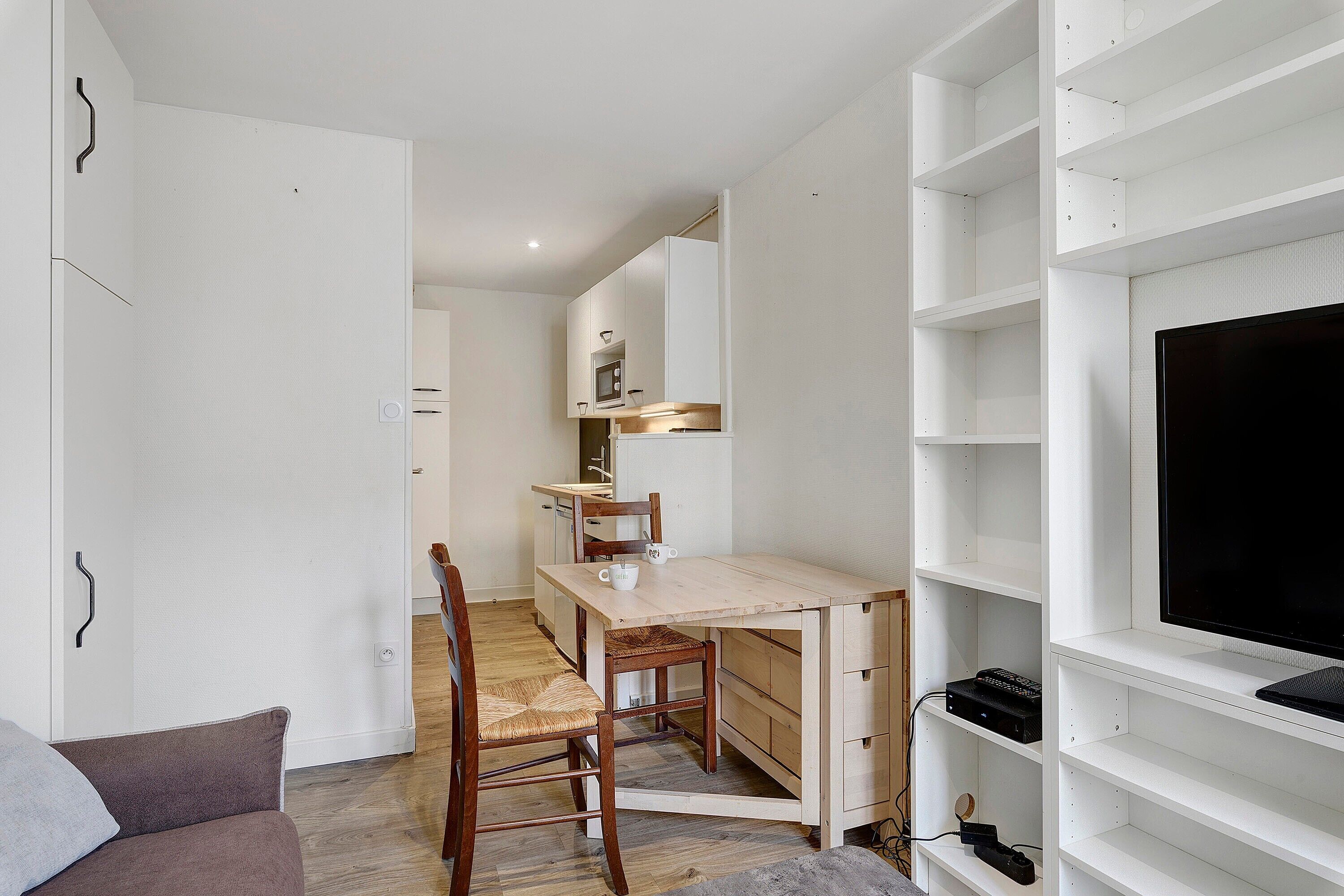 A compact living space with a kitchenette, a dining area, and a TV mounted on a white wall.