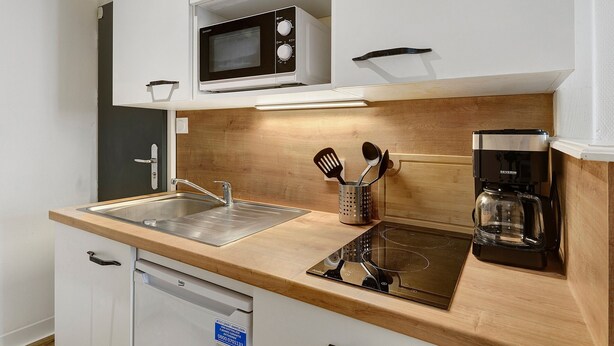 Una kitchenette compacta con microondas, cafetera y escurreplatos.
