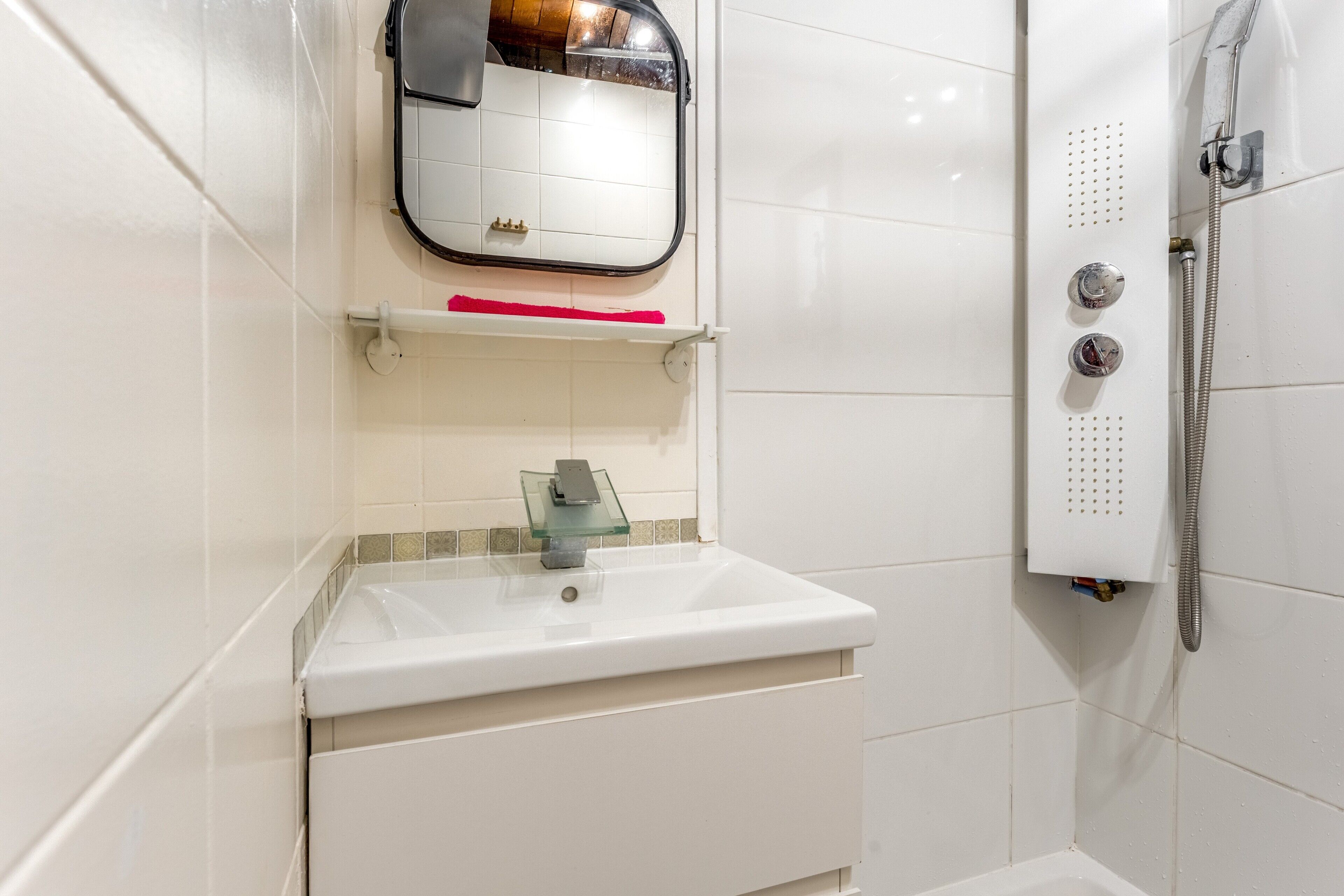 Een badkamer met een witte wastafel, spiegel en douche.
