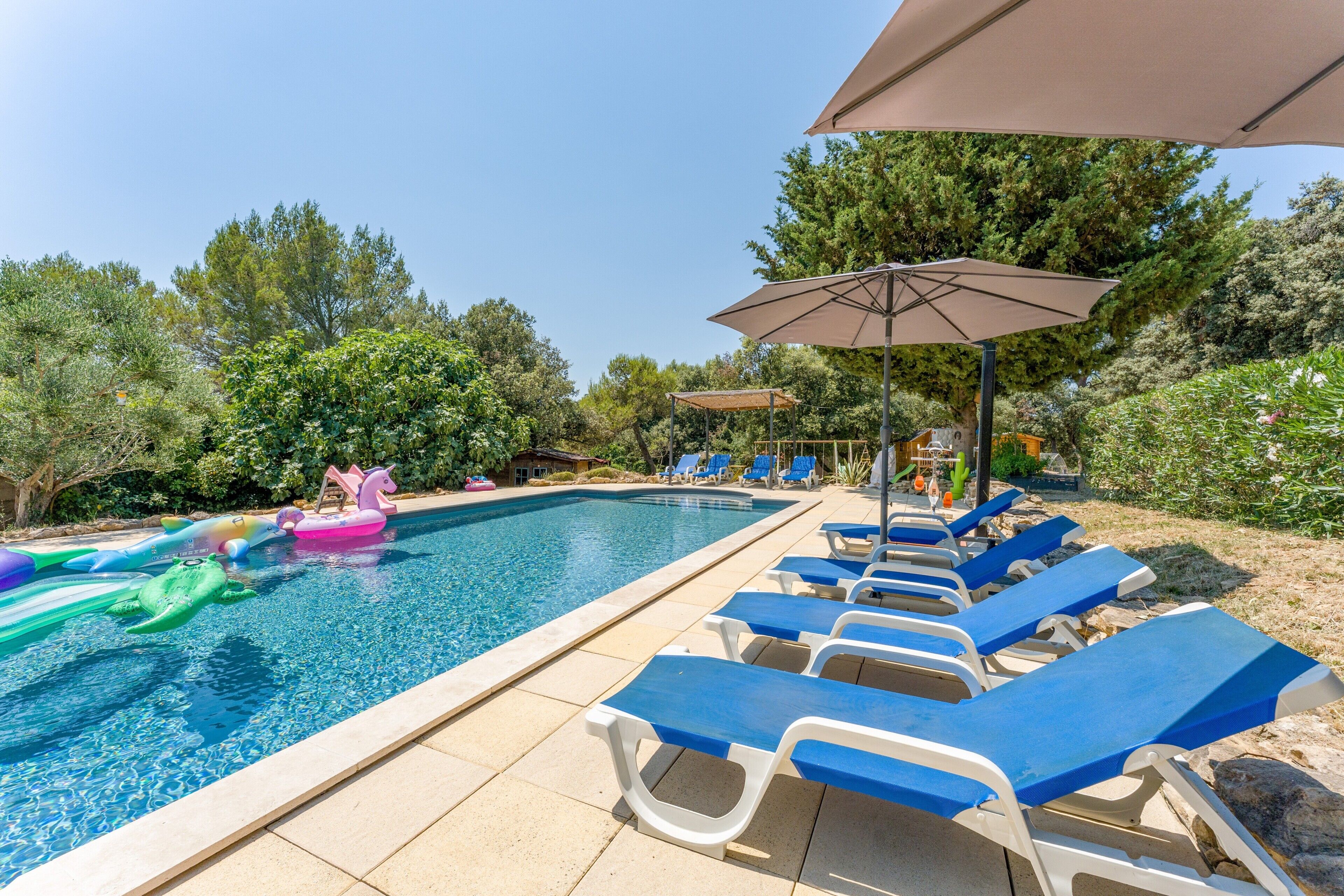 A swimming pool with lounge chairs and umbrellas, surrounded by trees.