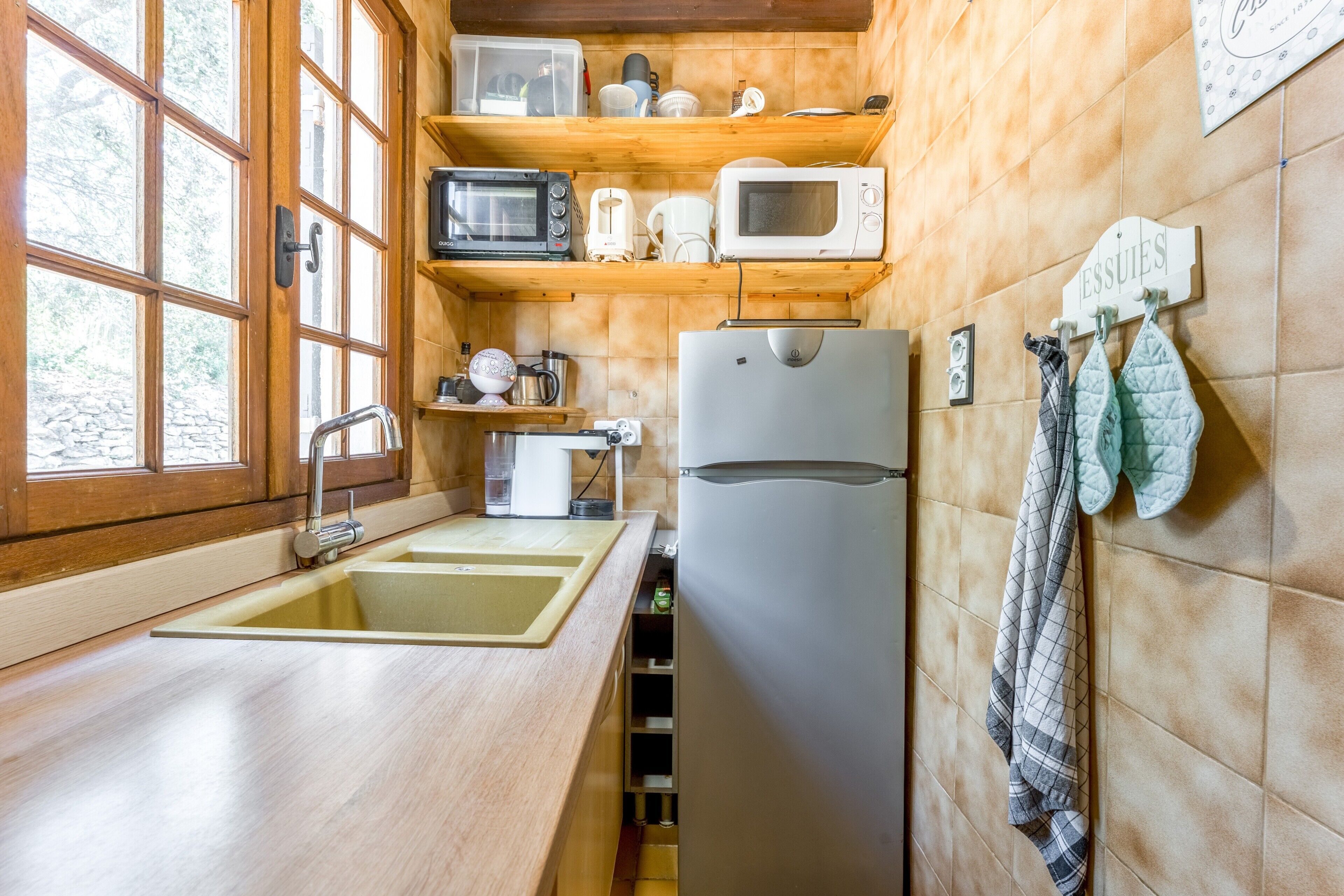 Cocina compacta con armarios de madera, un lavabo, un refrigerador y un microondas sobre una estantería.