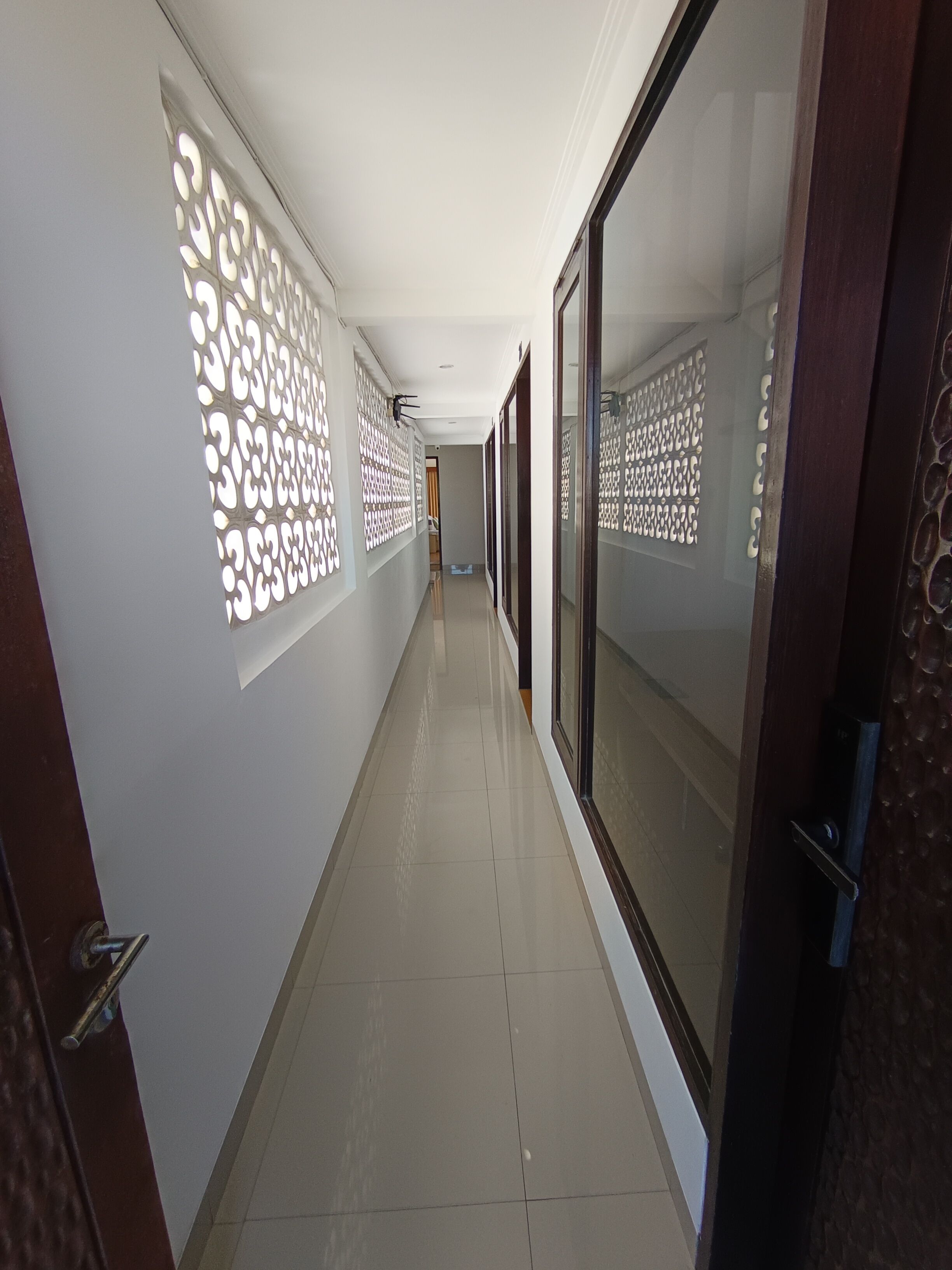 A corridor with patterned wall decorations, a tiled floor, and a door with a metallic handle.
