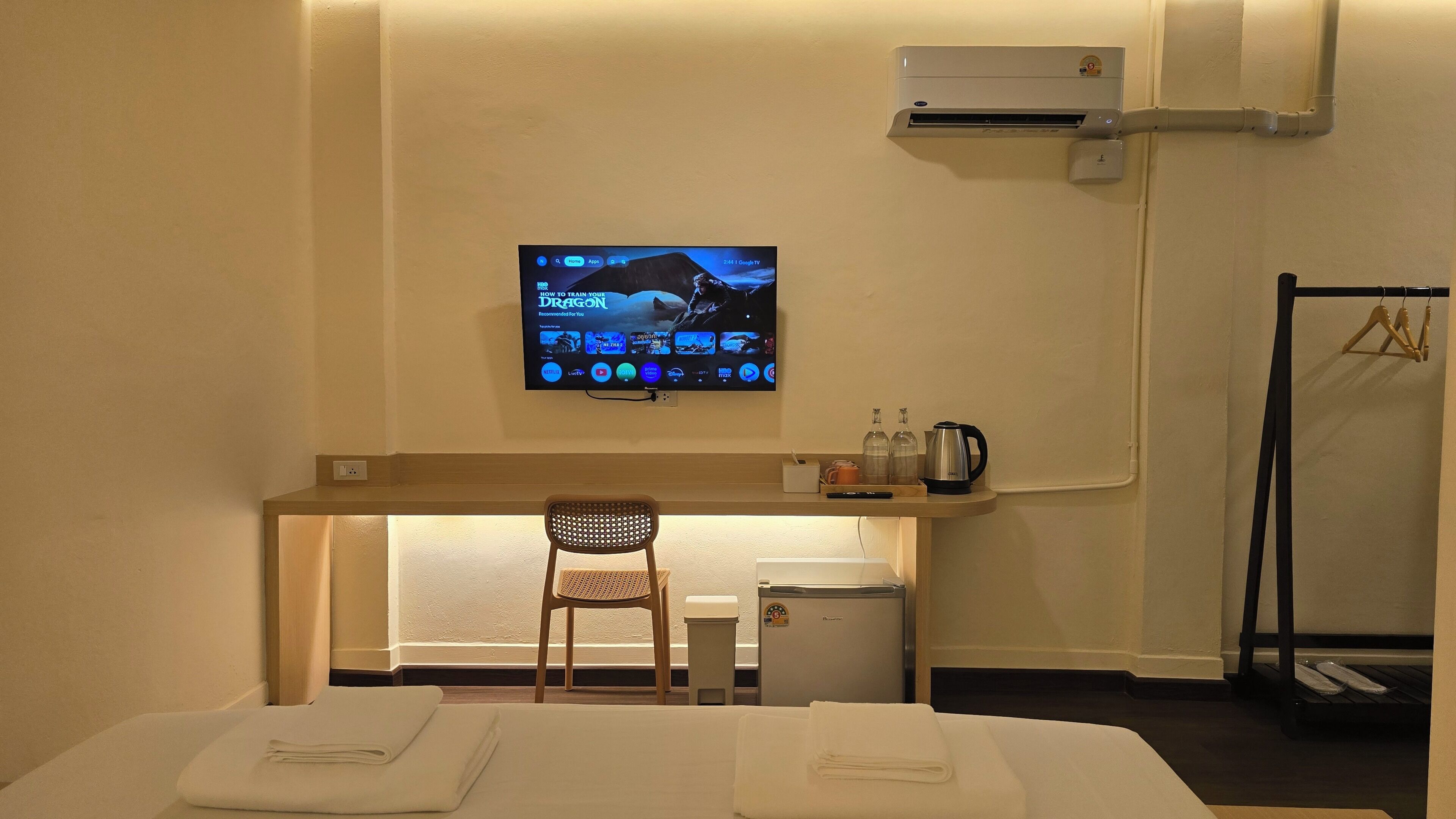 Habitación de hotel con cama, una silla, televisor montado en la pared, aire acondicionado y una mesita con tetera y vasos.