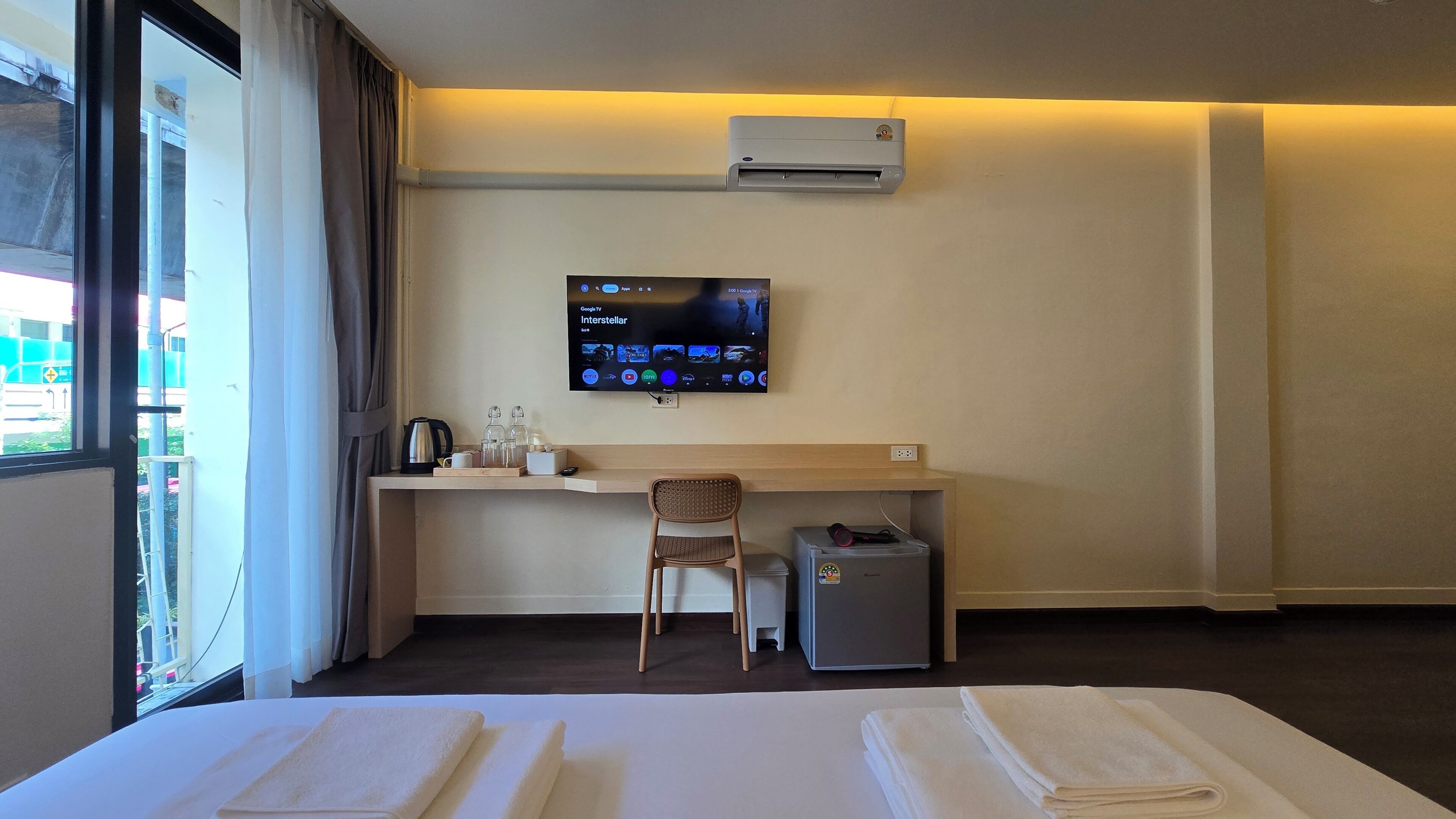 A hotel room with a bed, a desk with a chair, a television, and an air conditioning unit.
