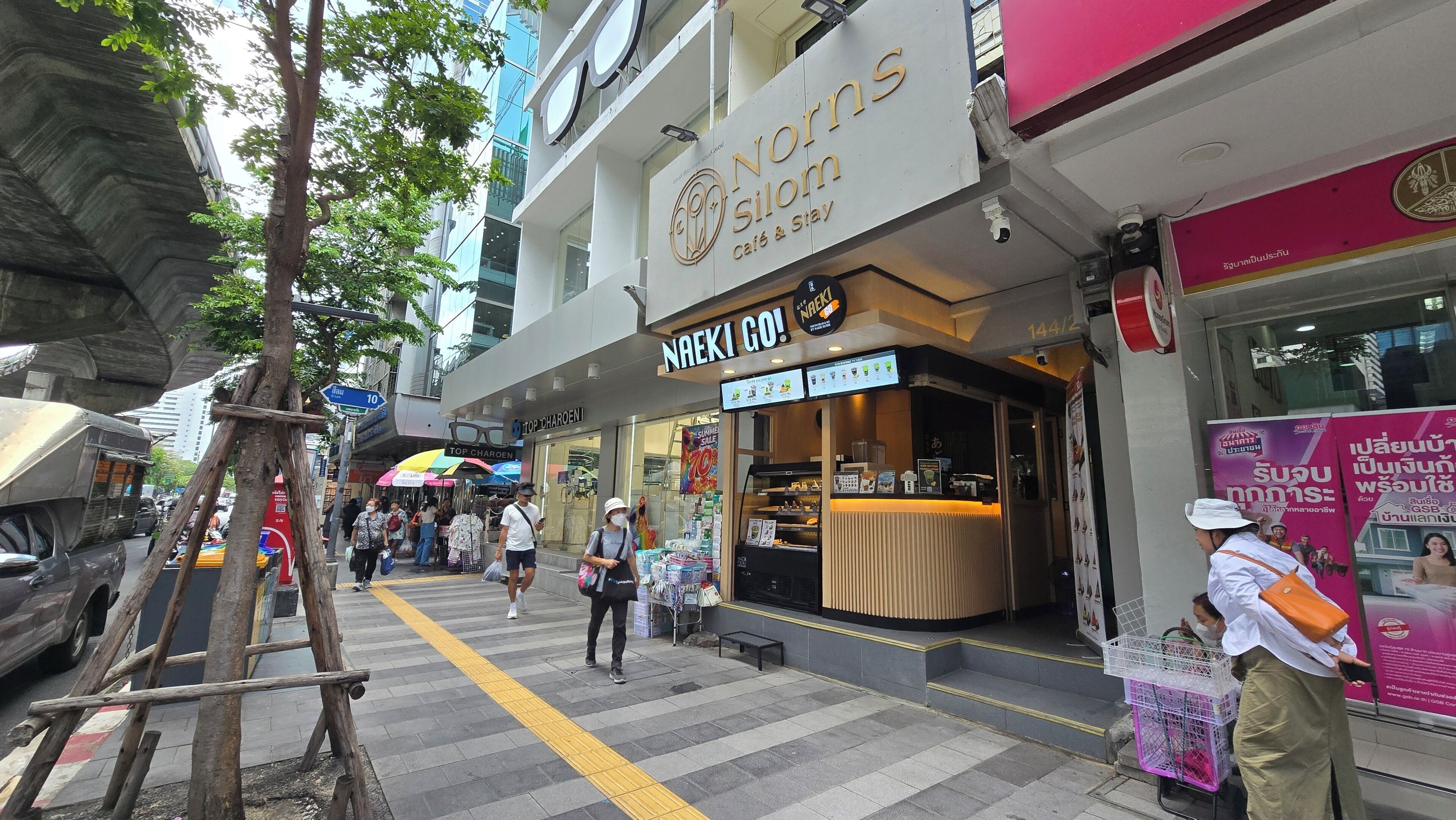 A street view with a cafe named 'Norma Silom' and a sign that says 'NAEKI GO!'.