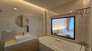 A modern bathroom with a large bathtub, a round mirror, and a built-in window. - Norns Silom Cafe & Stay (Bangkok)