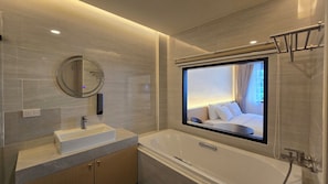 A modern bathroom with a large bathtub, a round mirror, and a built-in window.