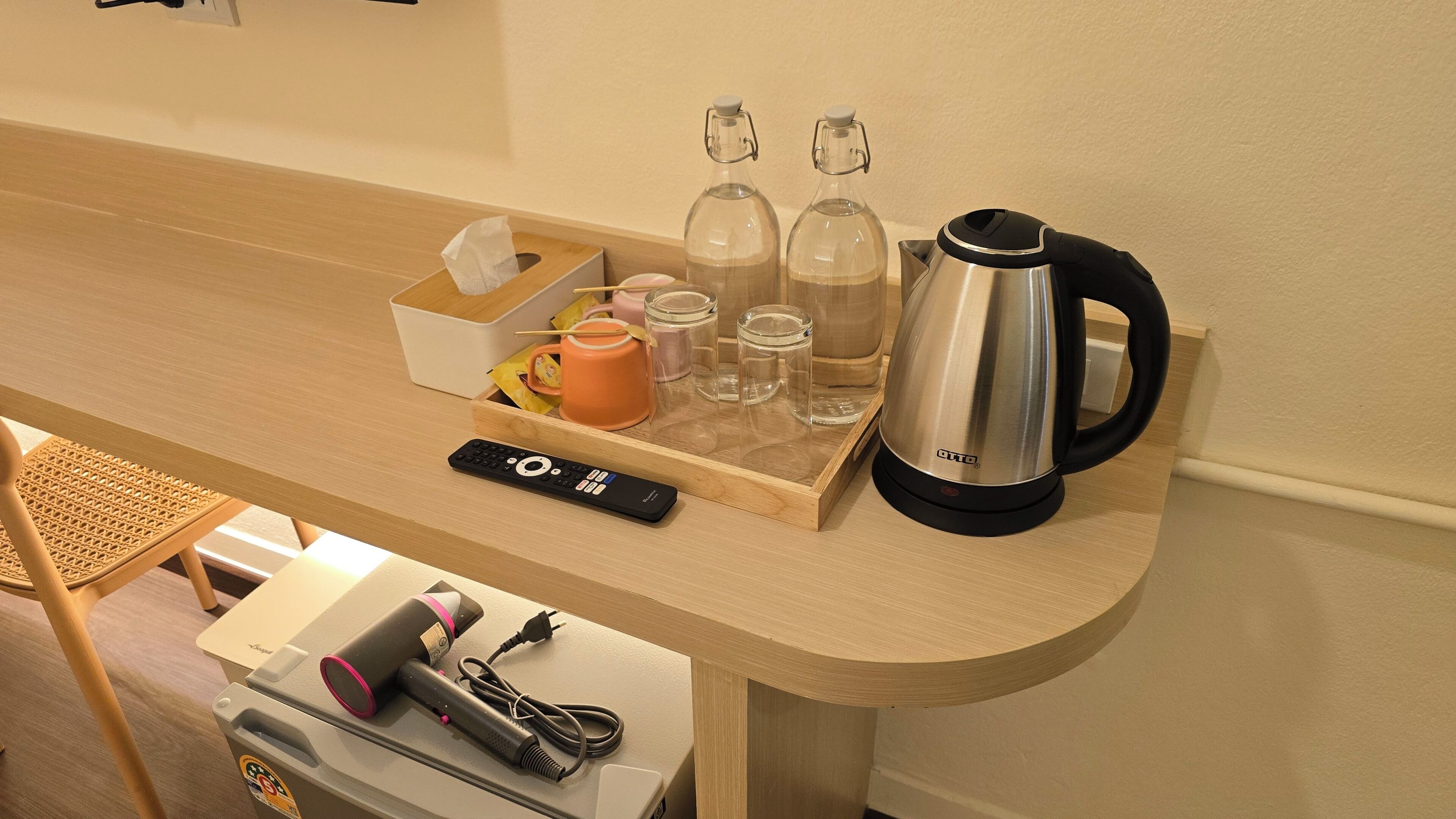 Een houten tafel met een waterkoker, een afstandsbediening en zakdoekjes.